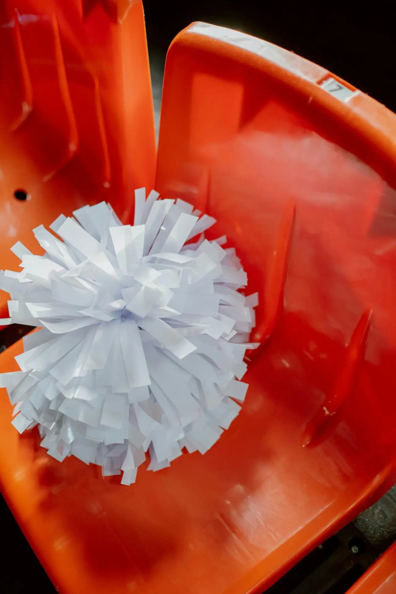 Close-up of a white pompom on a vibrant red stadium chair, highlighting sports spirit.