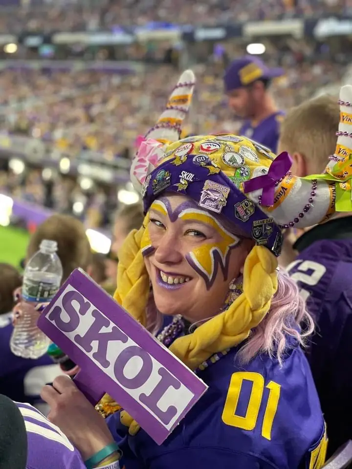 picture of Purplelicious wearing horns and facepainting at a football game, holding a sign that says SKOL 